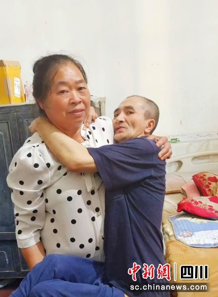 王明友抱丈夫坐轮椅。 邓建刚 摄 王明友抱丈夫坐轮椅。 邓建刚 摄